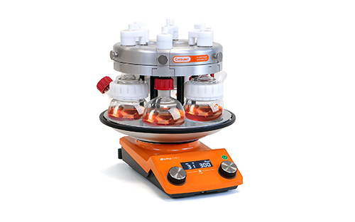 <center>Innovative Techniques for Sustainable Research with the Carousel 6</center> Carousel 6 Plus. At a slight angle, with orange liquid in the flasks.
